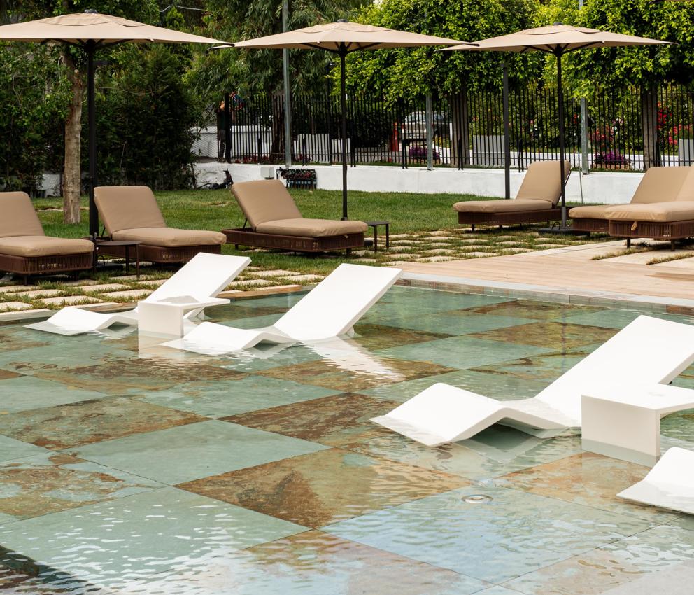 Eleganti lettini bianchi galleggiano su acqua limpida, circondati da ombrelloni e verde lussureggiante.