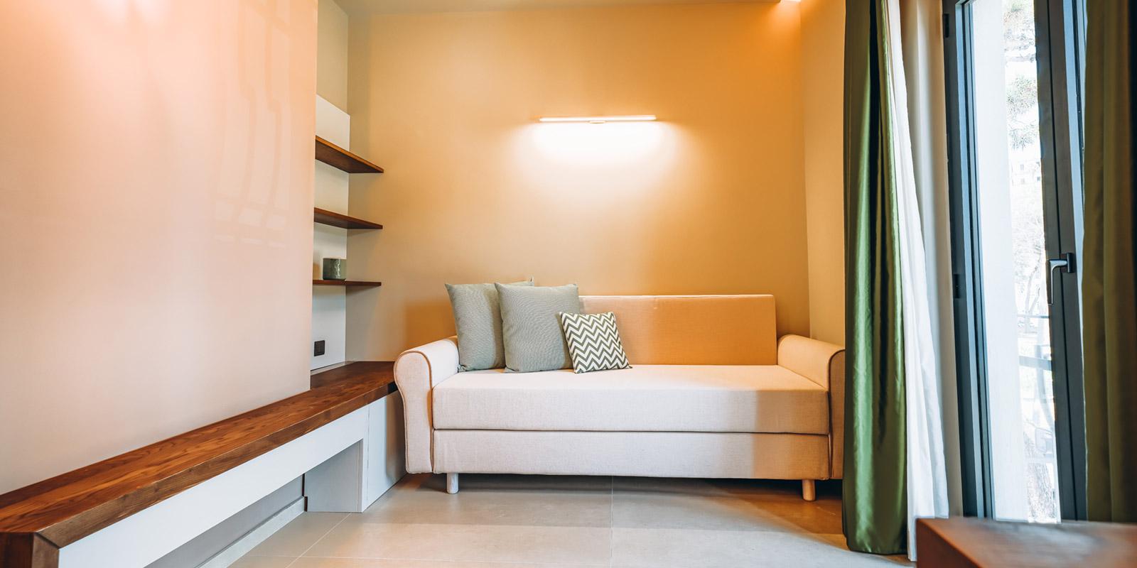 Soggiorno moderno con divano beige, mensole in legno e luce naturale.
