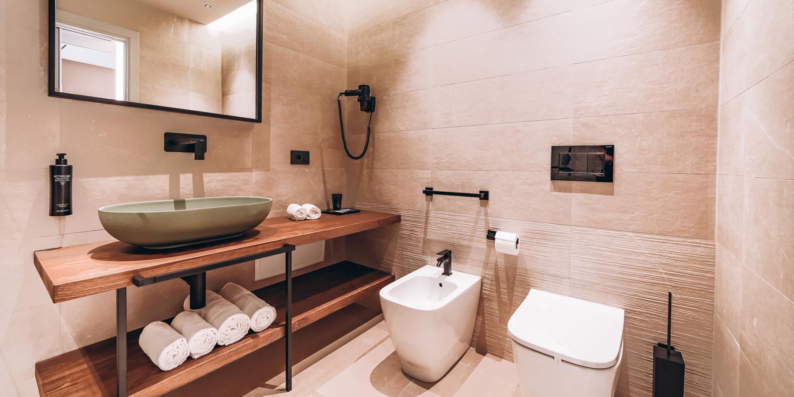 Bagno moderno con lavabo verde, specchio grande e sanitari eleganti su sfondo beige.
