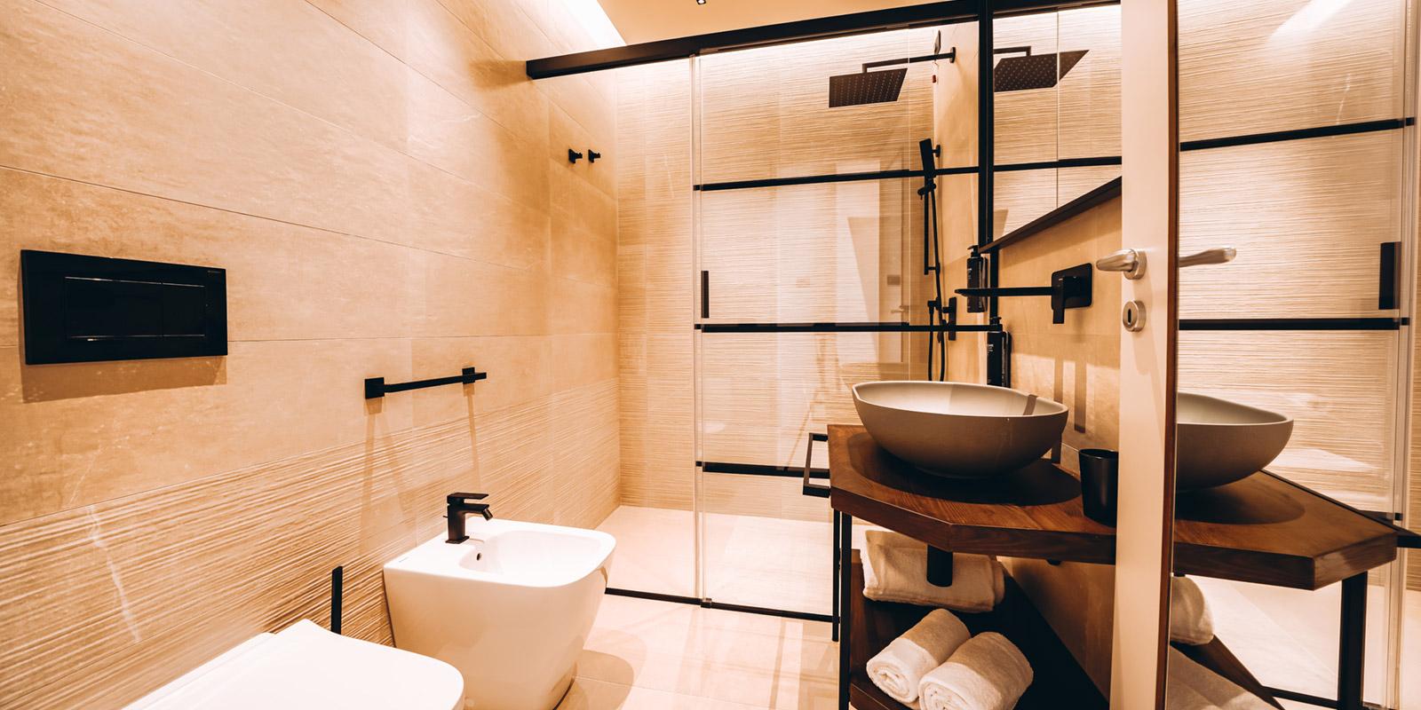 Bagno moderno con doccia, lavabo elegante, bidet e decorazioni minimaliste in tonalità calde.