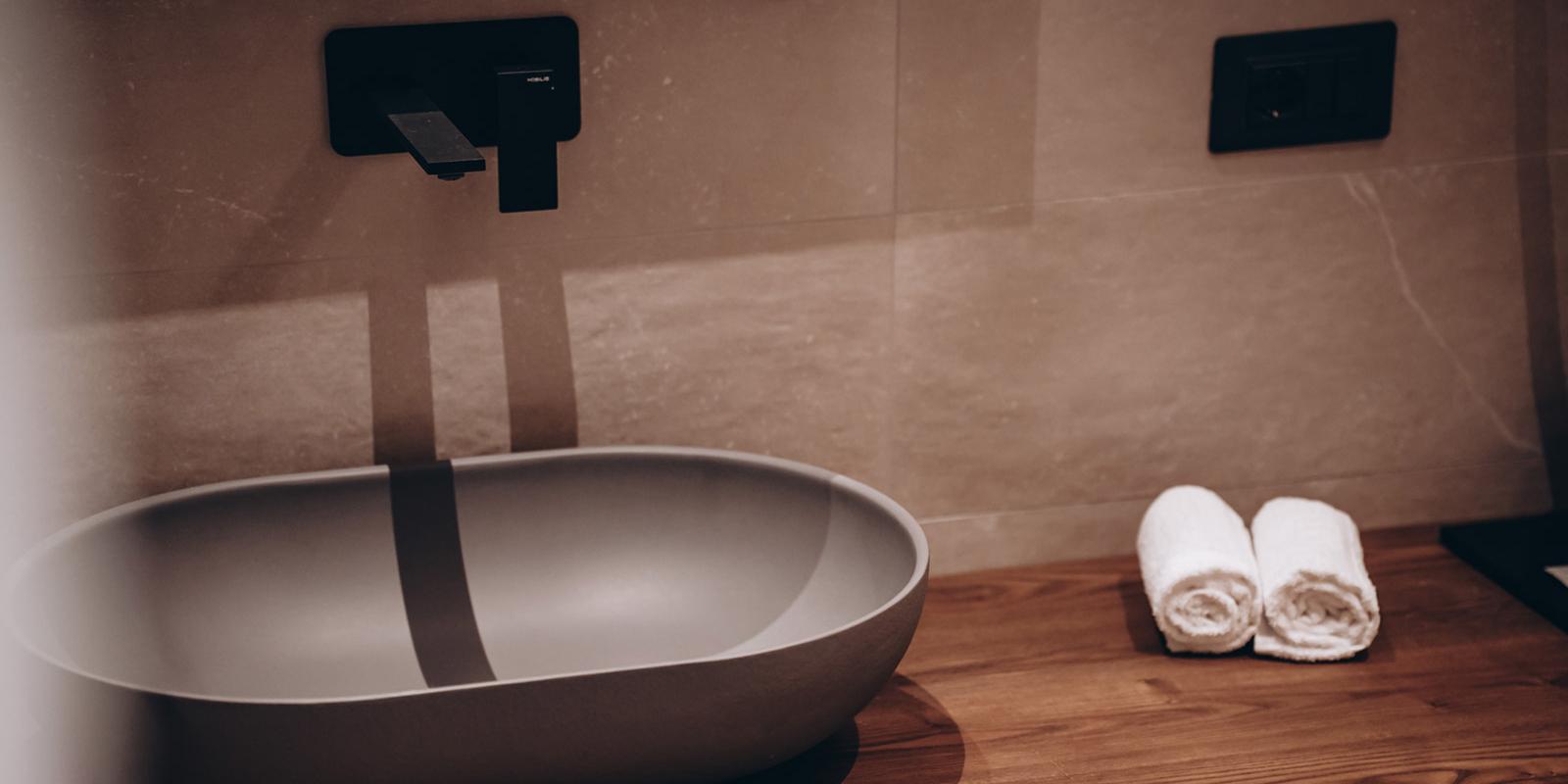 Lavabo moderno con rubinetto nero e asciugamani bianchi su mensola di legno.