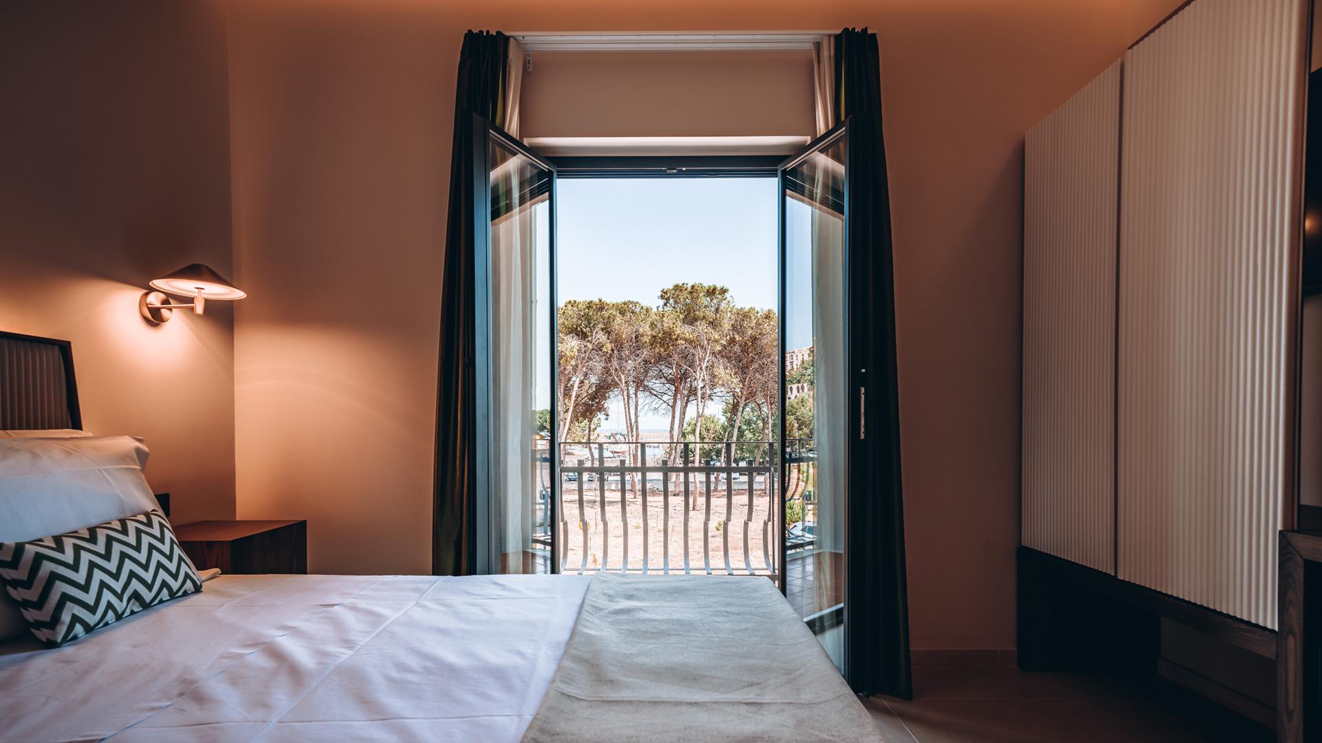 Camera da letto con balcone e vista su alberi, arredamento moderno e accogliente.