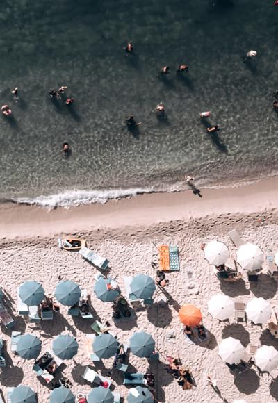 Spiaggia affollata con ombrelloni colorati e bagnanti in acqua vista dall'alto.