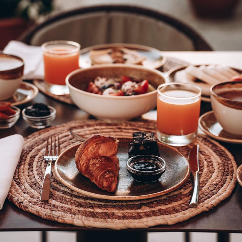 Colazione elegante con croissant, caffè, succo e dolci su tavola apparecchiata.